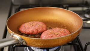hamburger patties cooking in a frying pan on the stove