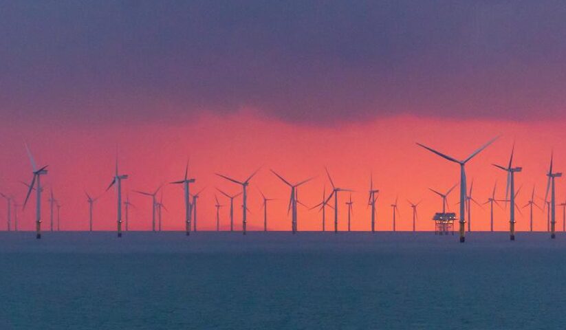 A vibrant sunset over an offshore wind farm captured from the coastline, highlighting renewable energy.