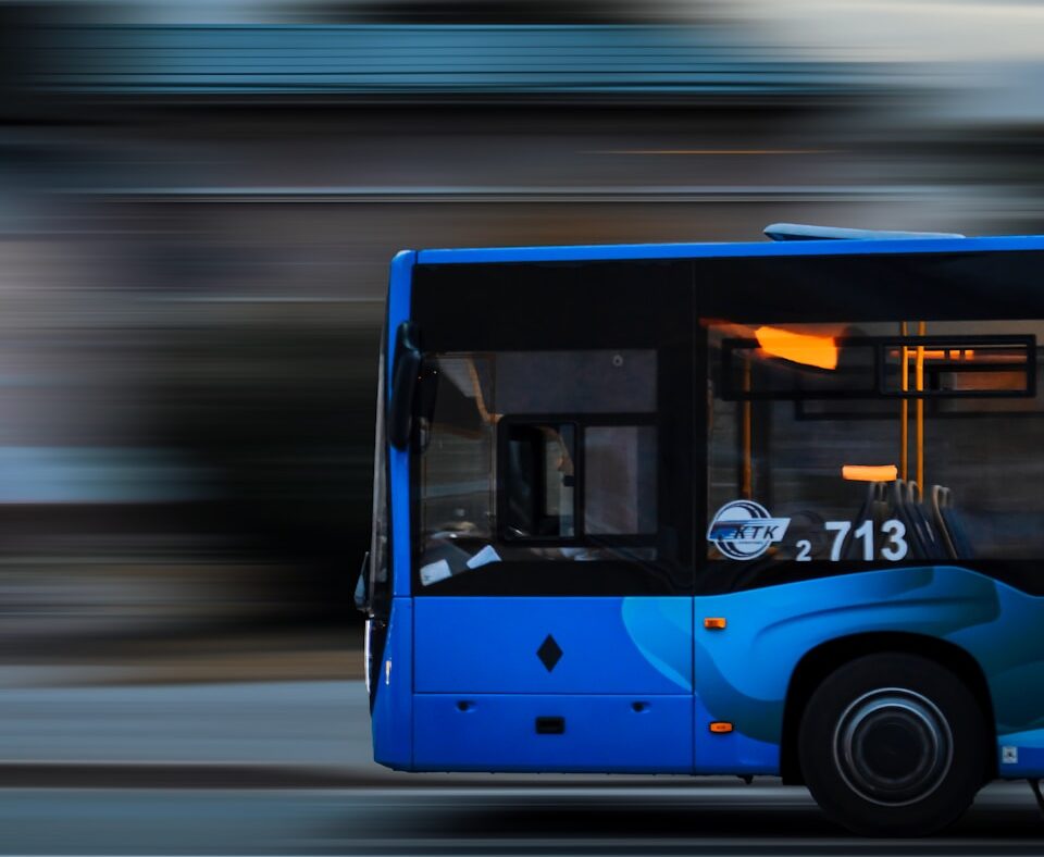 a blue bus driving down a street next to a tall building